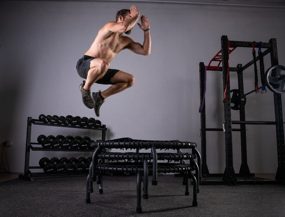 Man performing a box-jump on stacked JumpSport trampolines during a trampoline HIIT workout.