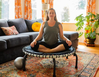 Woman sitting on a JumpSport wellness trampoline, representing calm and relaxation.