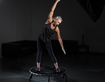 Active aging woman stretching on a JumpSport trampoline for senior balance training.