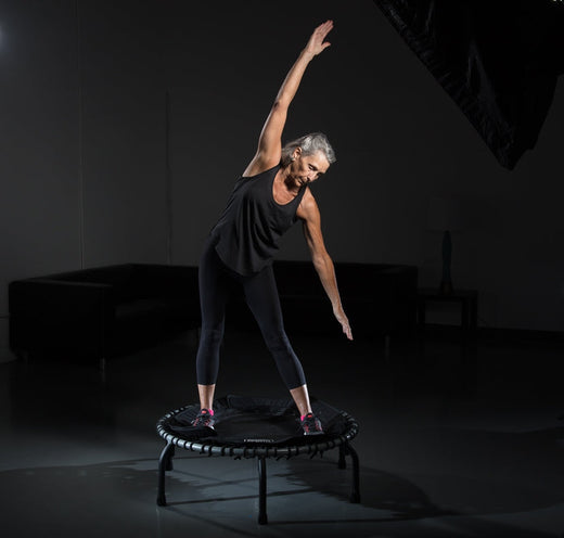 Active aging woman stretching on a JumpSport trampoline for senior balance training.